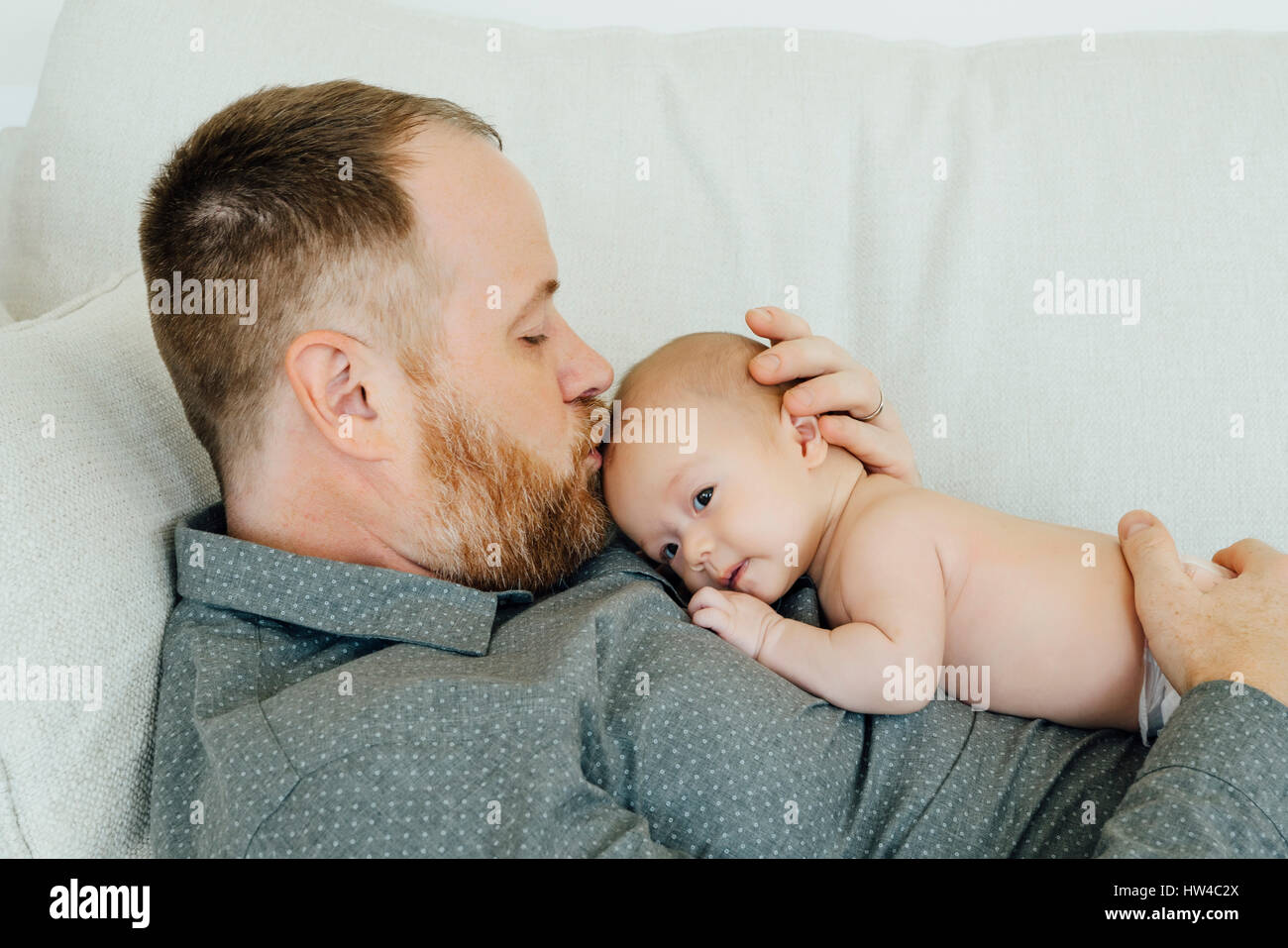 Vater Verlegung auf Sofa küssen Baby Tochter auf Kopf Stockfoto