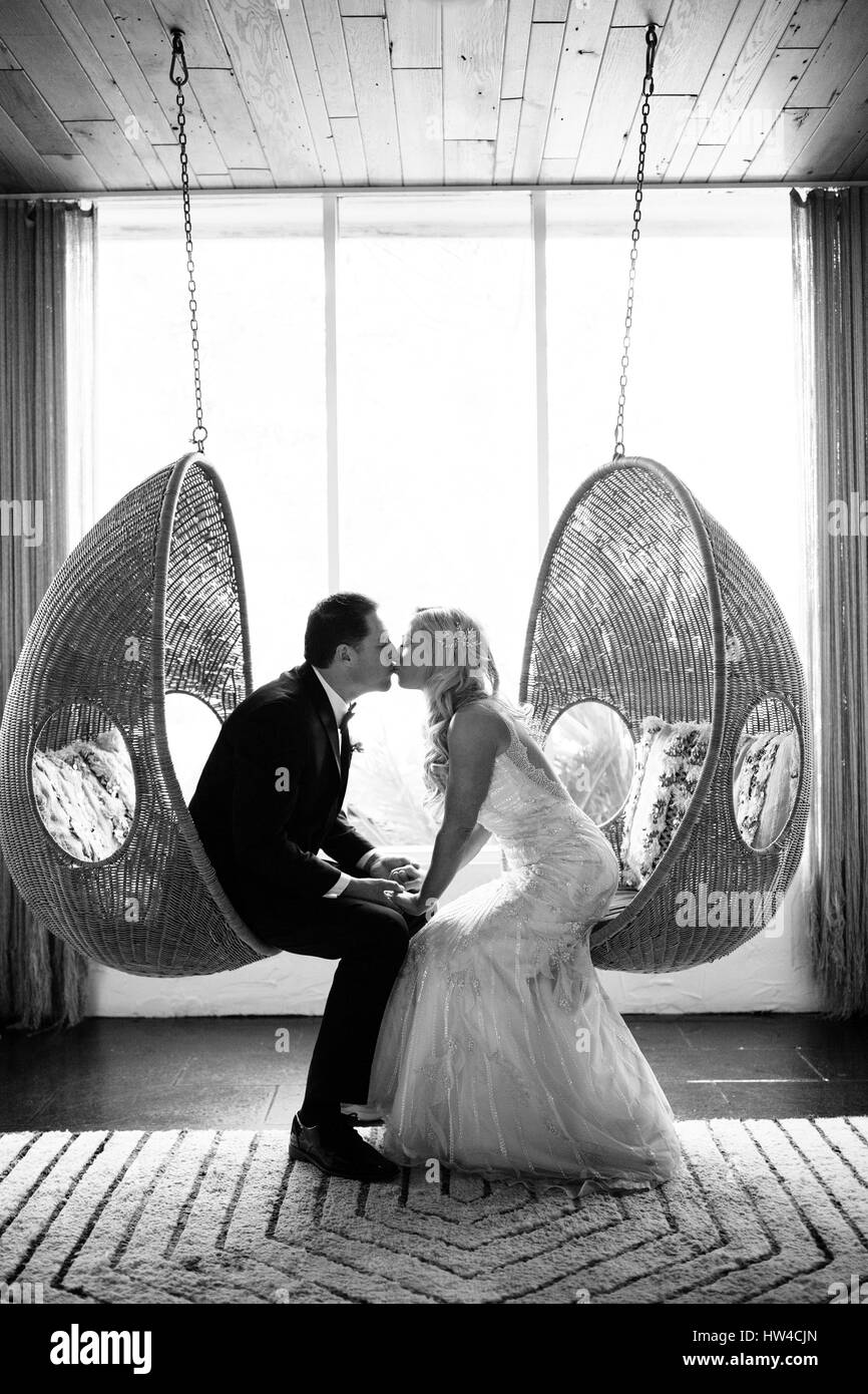 Kaukasische Braut und Bräutigam küssen in hängenden Stühlen Stockfoto