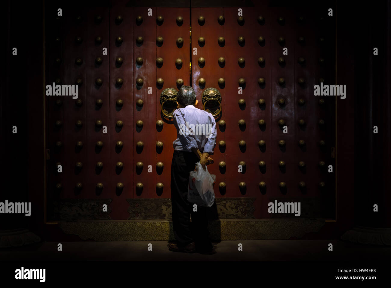 Ein älterer asiatischen Mann sieht aber die Lücke in den buddhistischen Tempeln riesigen roten Türen. Tooth Relic Temple, Chinatown, Singapur. Stockfoto