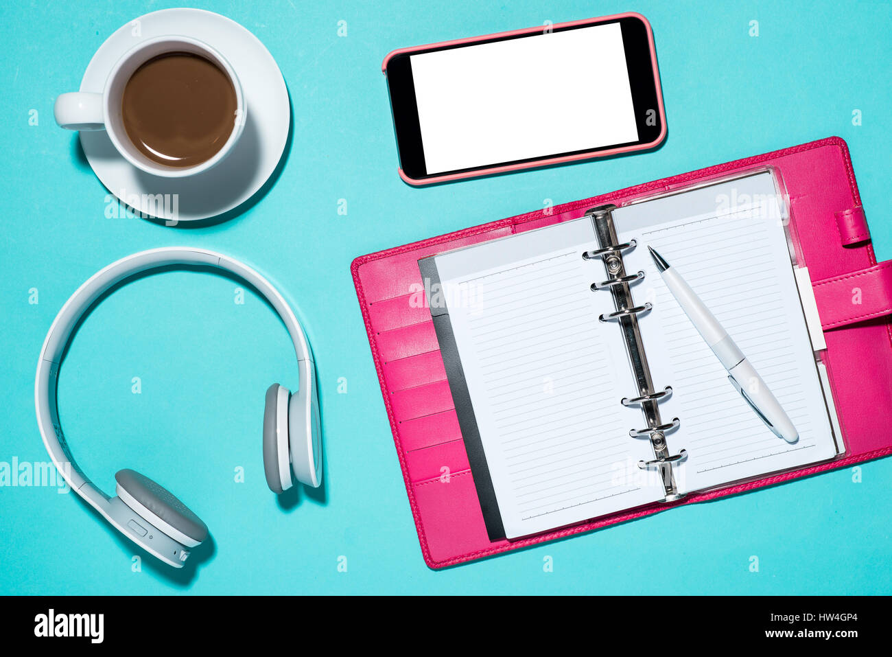 Büromöbel und Bürobedarf. Draufsicht auf geöffneten Notizbuch, Stift, Kopfhörer, Smartphone und Tasse Kaffee auf blau. Stockfoto