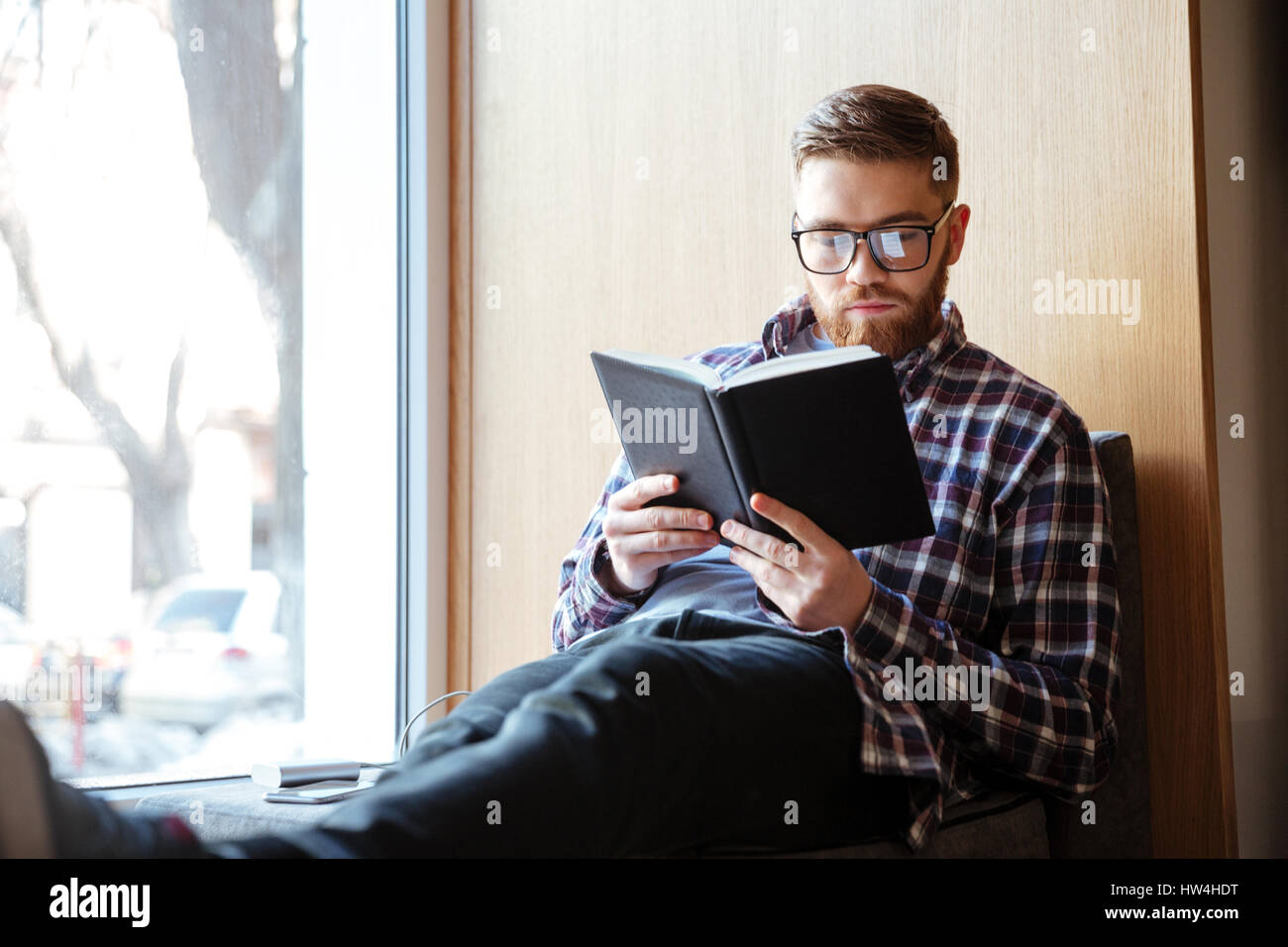 Junge männliche Schüler sitzt auf der Fensterbank in Bibliothek und lesen Buch Stockfoto