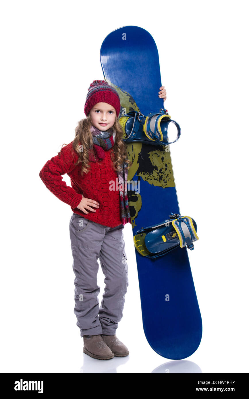 Kleines Mädchen mit lockige Frisur tragen, gestrickte Pullover, Schal, Mütze und Handschuhe mit blauen Snowboard lächelnd, isoliert auf weiss. Daumen nach zeigen oben. Gewinnen Stockfoto