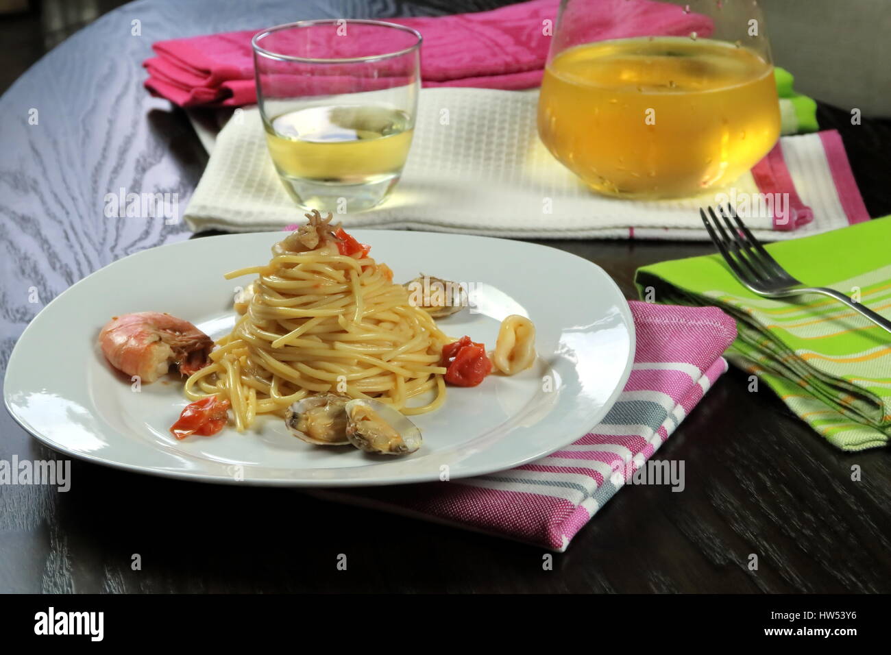 Pasta mit Meeresfrüchten in weißen Schale auf bunte Küchentücher und kühlen Weißwein (Glas und Karaffe) im Hintergrund. Italienische Spaghetti allo Scoglio Rezept Stockfoto