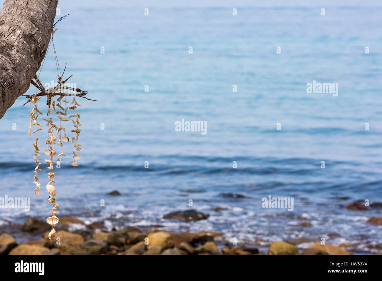Eine handgemachte Meer Shell mobile hängen von einer Palme Strand mit ruhigen Meer im Hintergrund mit Schärfentiefe. Stockfoto