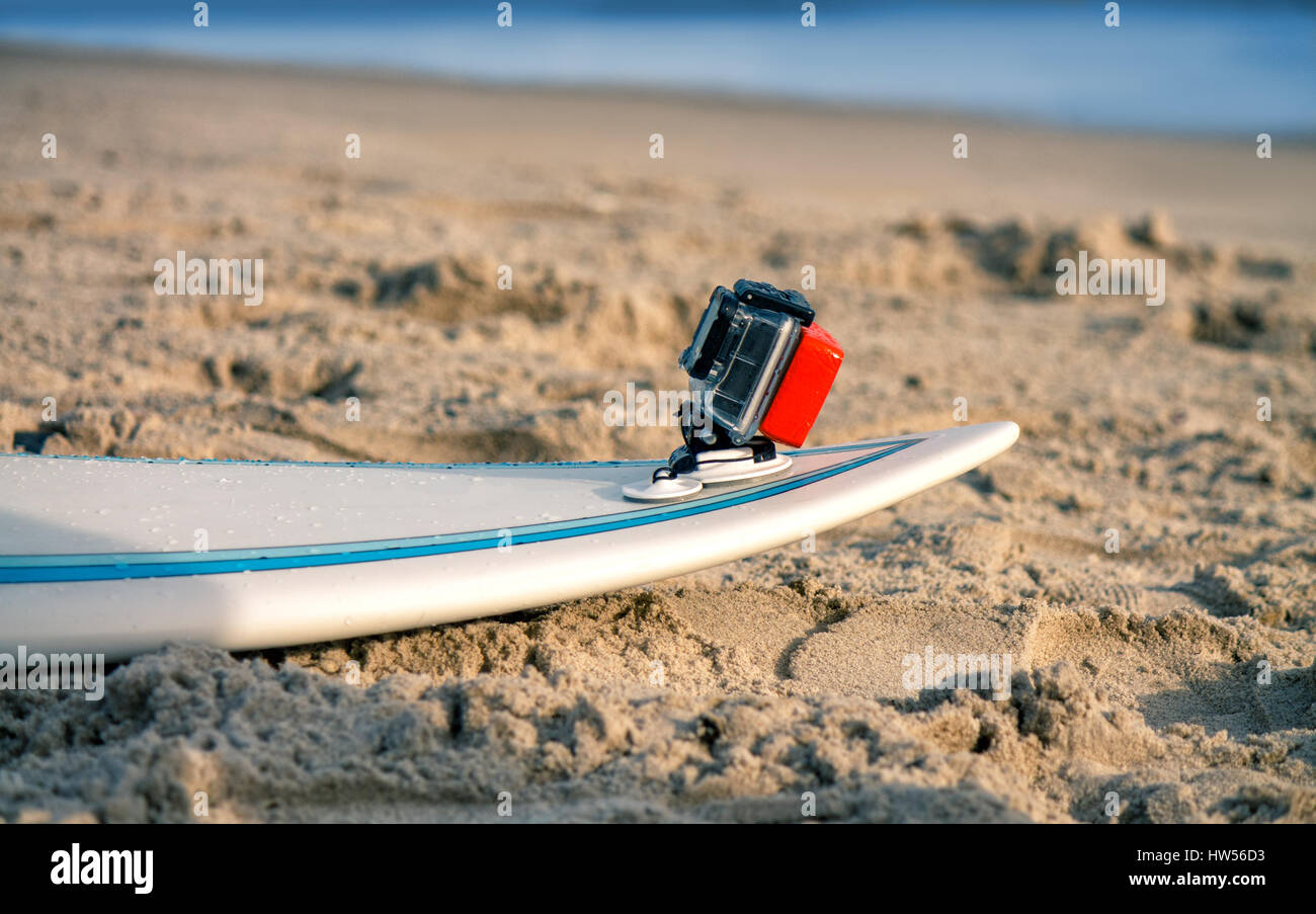 Surfbrett mit angehängten Action-Kamera liegt auf dem Sand am Strand. Action-Kamera ist im wasserdichten Gehäuse zum Schwimmen. Stockfoto