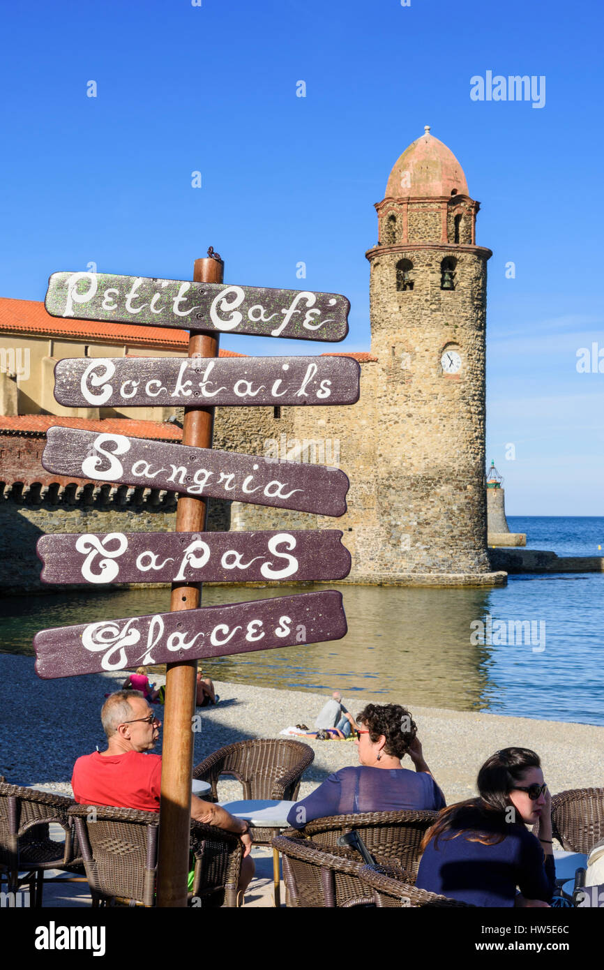 Konzentrieren Sie sich auf ein Café-Schild an ein Strandcafé, überragt von der Glockenturm der Kirche von Notre Dame des Anges, Collioure, Côte Vermeille, Frankreich Stockfoto