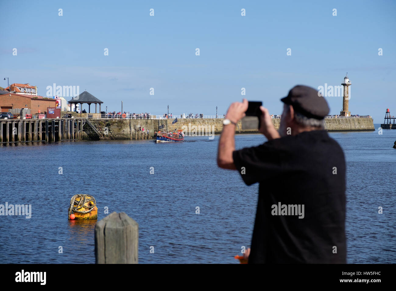 Mann beobachtet ein Segelboot kommend in den Hafen von Whitby Stockfoto