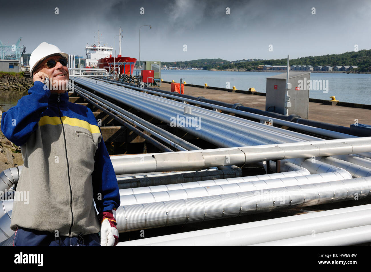 -MODELL VERÖFFENTLICHT. Ingenieur auf Handy mit Pipelines im Hintergrund. Stockfoto