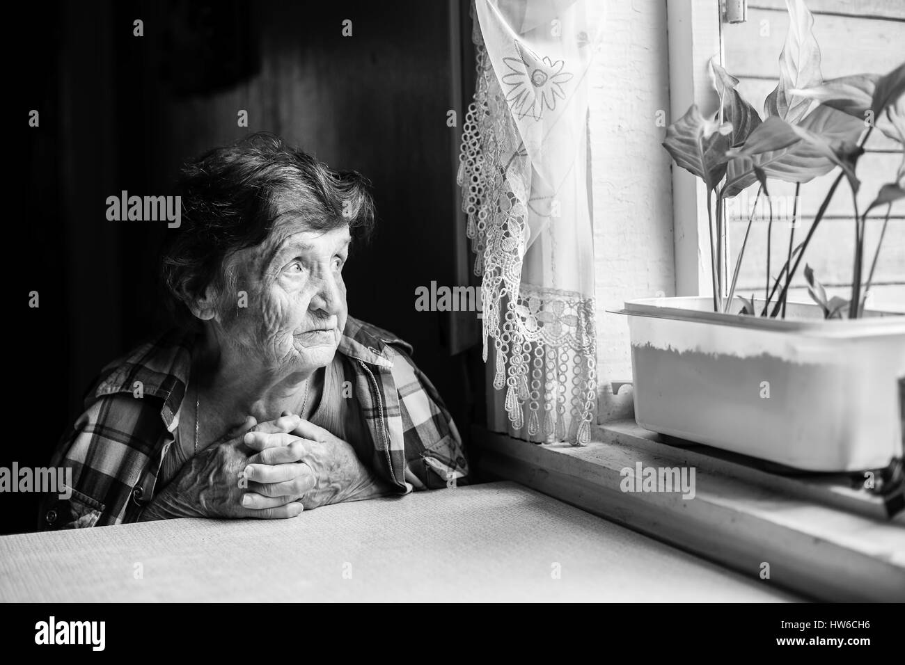 Eine ältere Frau, die Sehnsucht am Fenster. Schwarz-weiß-Foto. Stockfoto