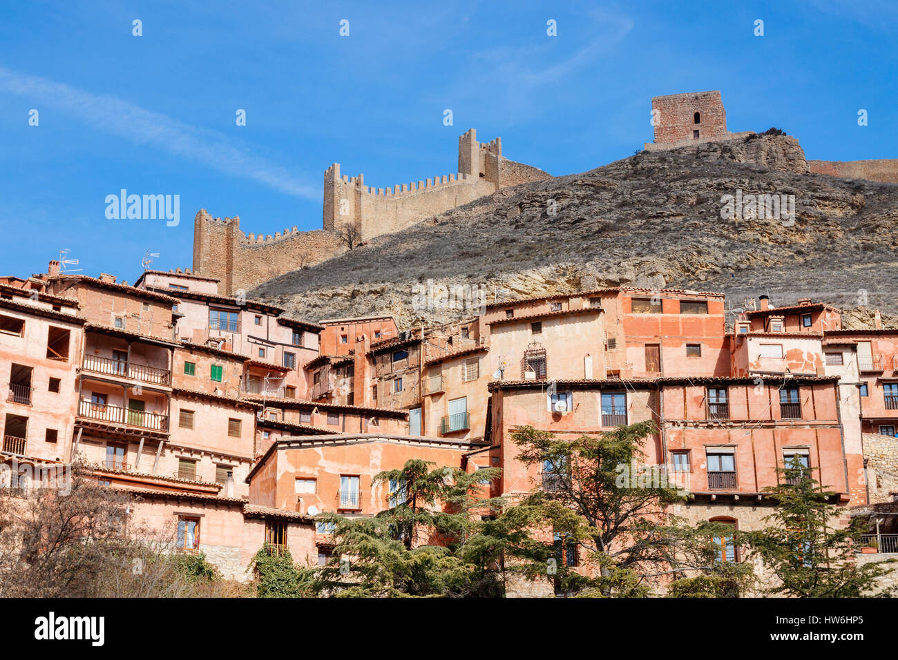 Häuser und Straßen von Albarracin gegen den Hang des Hügels mit der Stadtmauer auf der Oberseite an einem sonnigen Tag unter einem blauen Himmel. Albarracin, Teruel, Spanien. Stockfoto