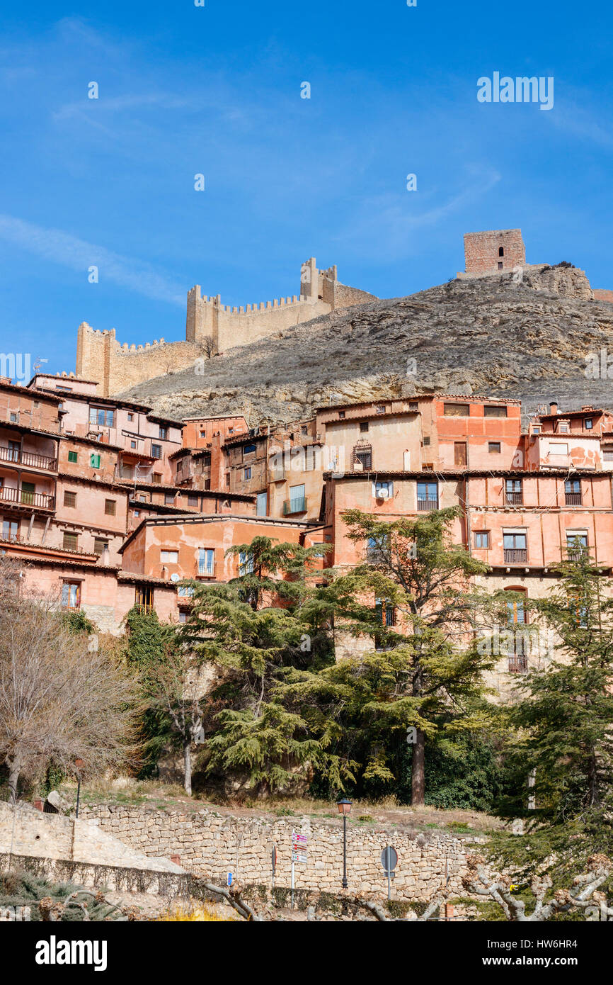 Häuser und Straßen von Albarracin gegen den Hang des Hügels mit der Stadtmauer auf der Oberseite an einem sonnigen Tag unter einem blauen Himmel. Albarracin, Teruel, Spanien. Stockfoto