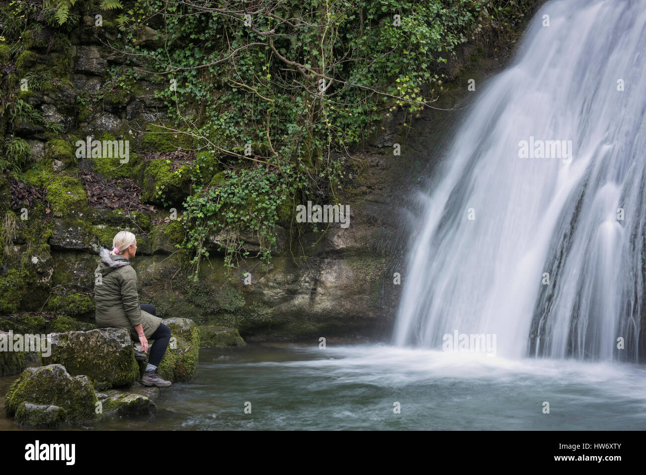 In Gedanken versunken, sitzt eine Dame auf einem Felsen am Fuße des Janets Foss, eine idyllische, unberührte, Wasserfall und Teich - in der Nähe von Malham, Yorkshire Dales, England. Stockfoto