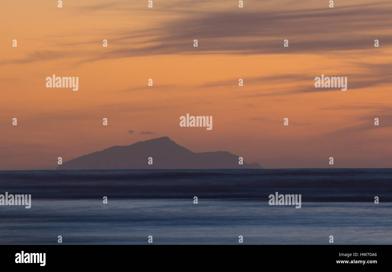 Das letzte Licht des Tages an einem Strand mit einer Insel in der Ferne. Stockfoto