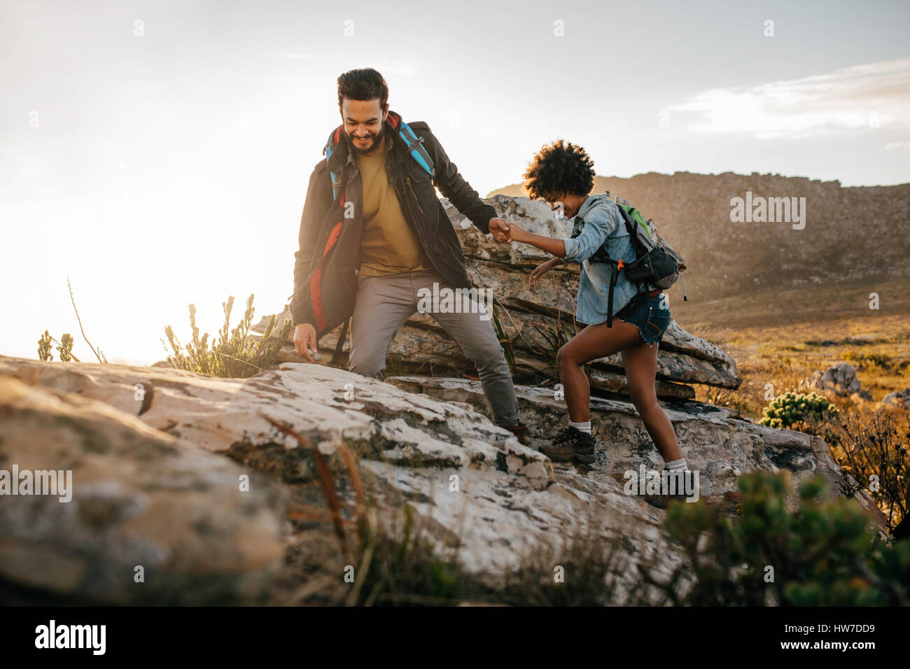 Junger Mann hilft Freund zu dem Felsen erklimmen. Junges Paar Wanderungen in der Natur. Stockfoto