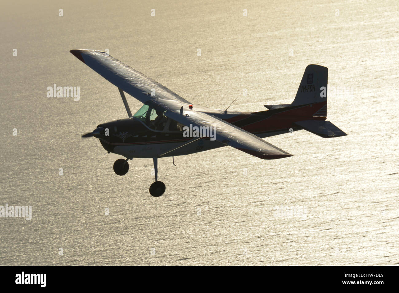 Cessna 180 Skywagon Flugzeug Flugzeug in der Silhouette, Hintergrundbeleuchtung durch die Reflexion der Sonne abseits des Ozeans. Stockfoto