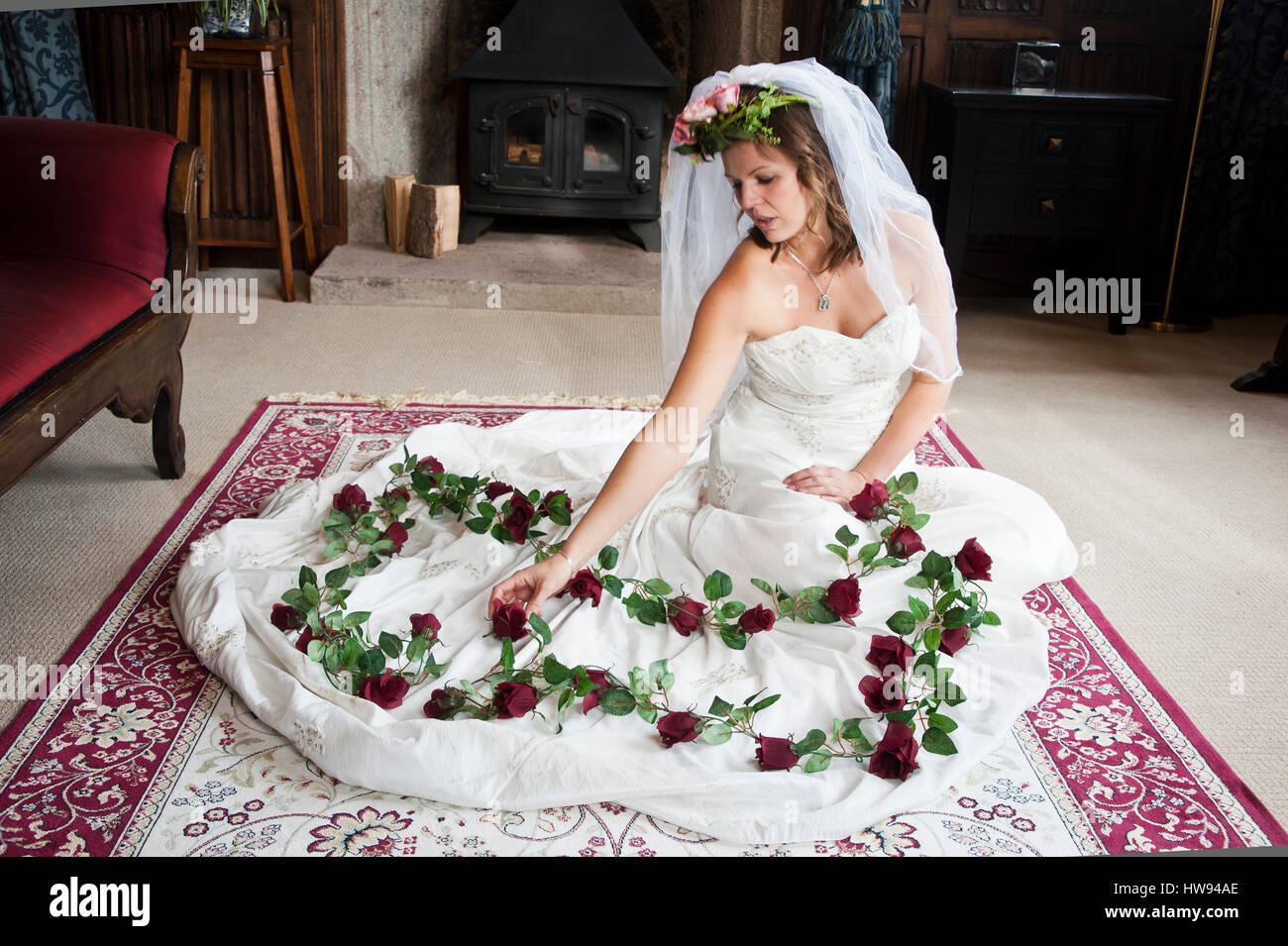 Frau trägt ein Brautkleid mit Rosen auf einem Teppich knieend über das Skit  ihres Kleides gelegt Stockfotografie - Alamy