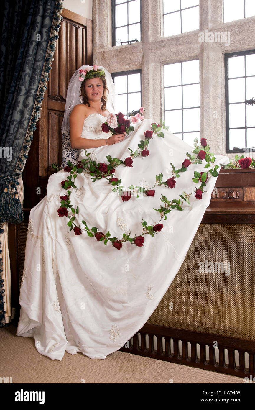 Frau trägt eine Brautkleid mit Rosen drapiert über ihm, auf einen Platz am  Fenster sitzen Stockfotografie - Alamy