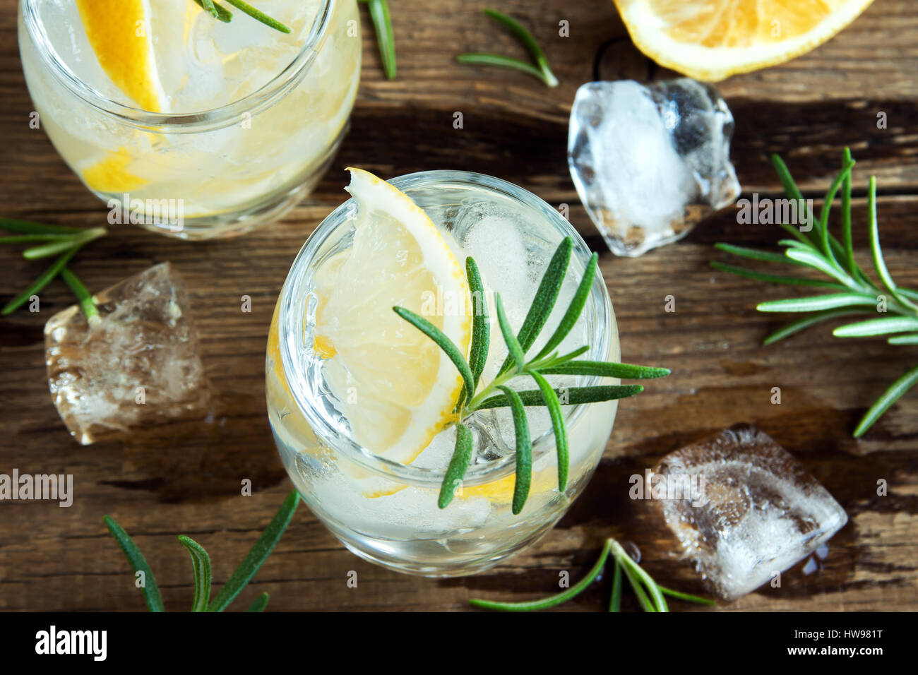 Alkoholische Getränke (Gin Tonic Cocktail) mit Zitrone, Rosmarin und Eis am rustikalen Holztisch, Textfreiraum Stockfoto