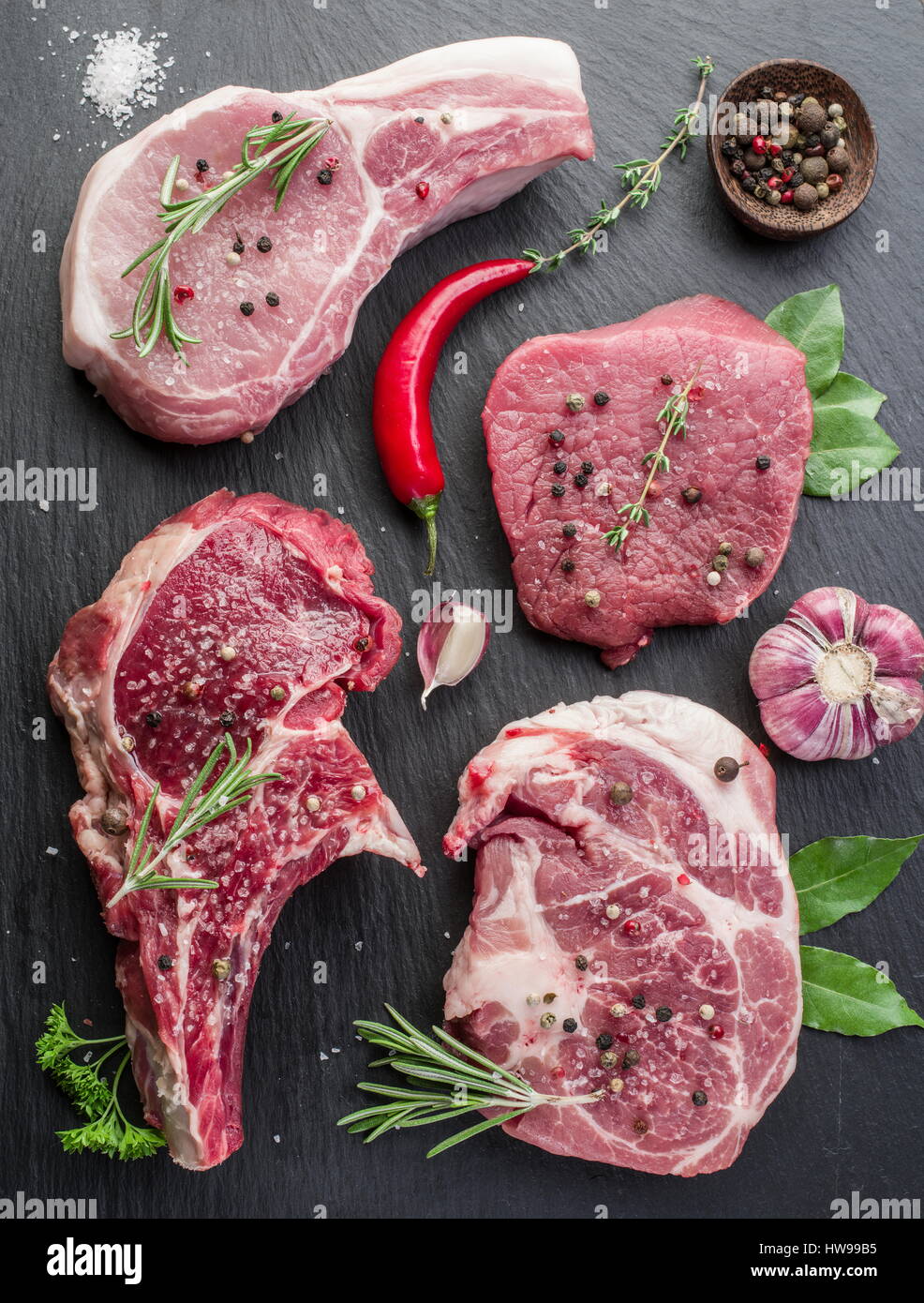 Rohes Fleisch Steaks mit Gewürzen auf dem schwarzen Schneidebrett. Stockfoto