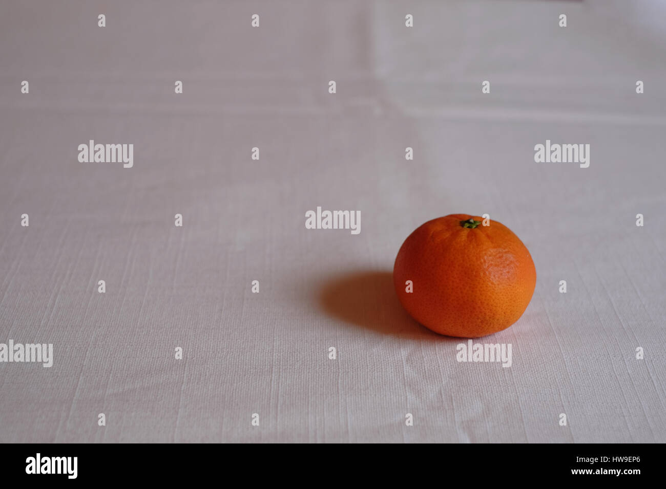 Einer einzigen Mandarine auf einer weißen Tischdecke Stockfoto