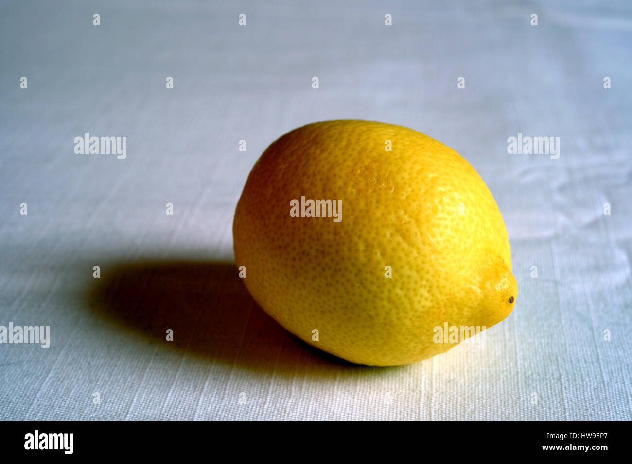 Eine einzelne Zitrone auf ein weißes Tischtuch Stockfoto