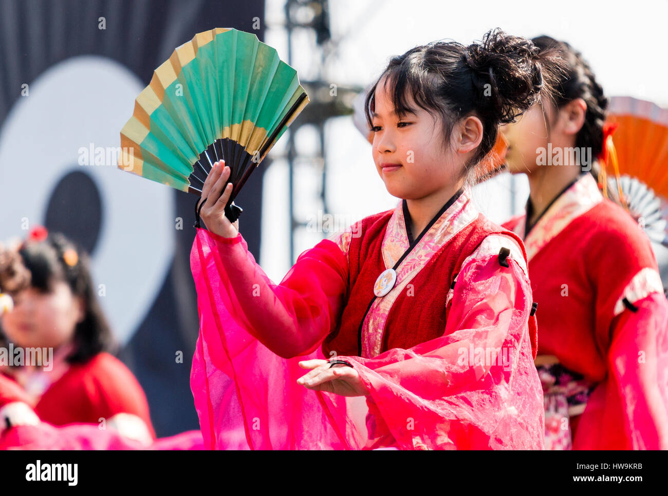 Hinokuni Yosakoi Dance Festival. Schließen oben. Kind, Mädchen in rosa Kostüm mit transparenten Ärmeln und Holding Grün Lüfter. Andere Tänzer im Hintergrund. Stockfoto