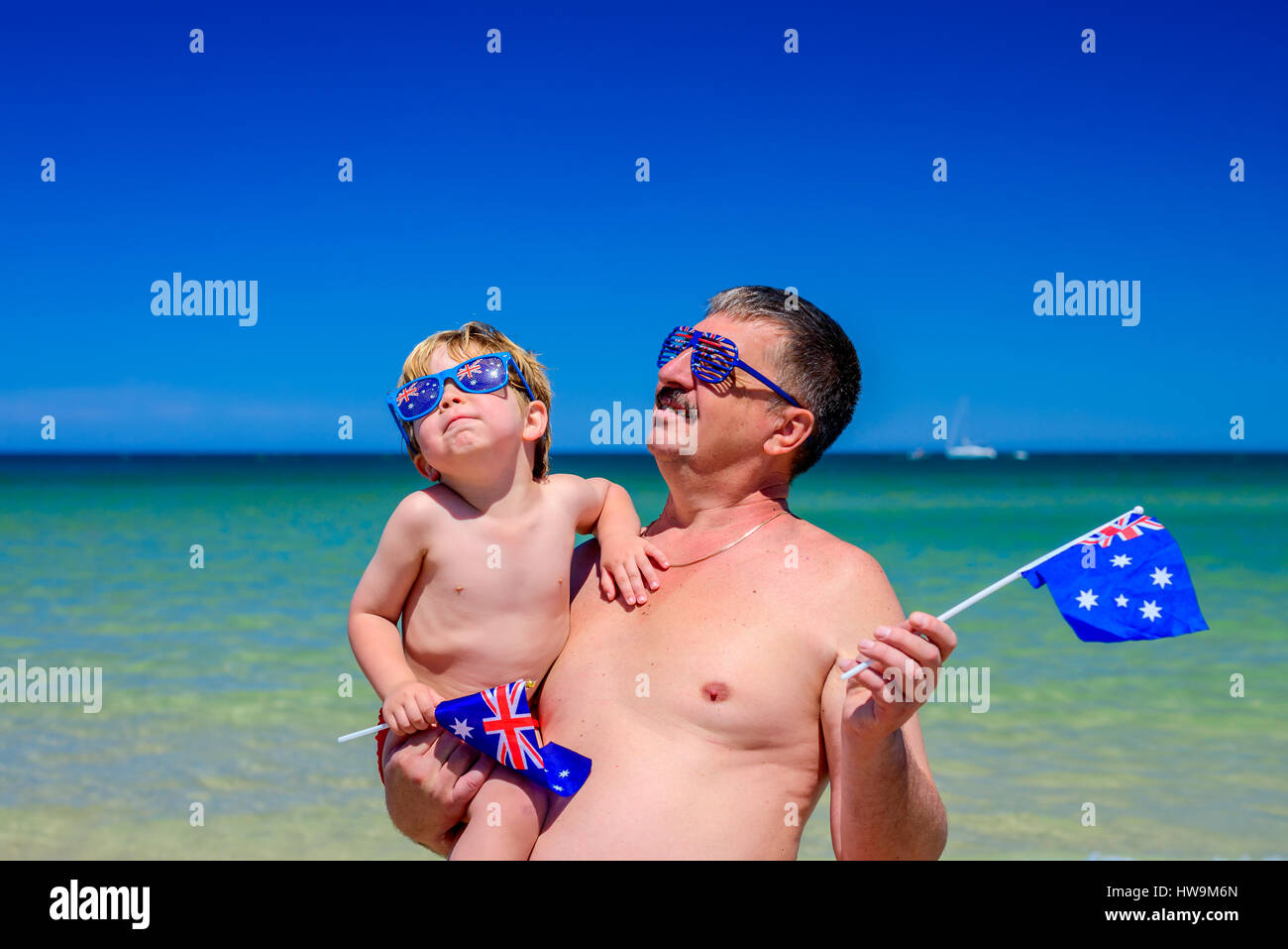 Niedlichen lächelnde junge mit seinem Großvater und australische Flaggen stehen am Strand am Australia day Stockfoto