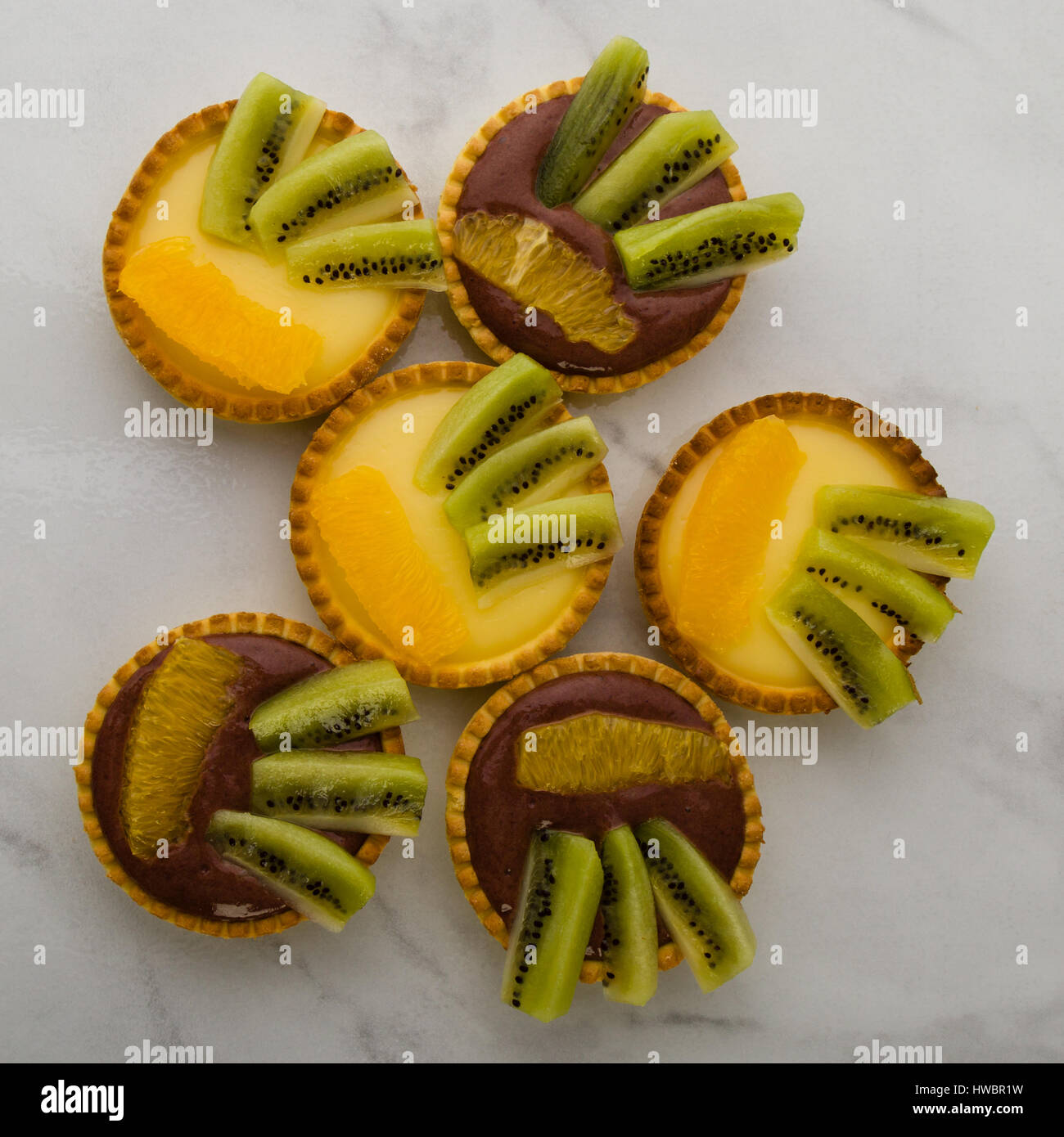 Runde, Vanille und Schokolade Törtchen mit Kiwi und Orange auf Tisch Stockfoto