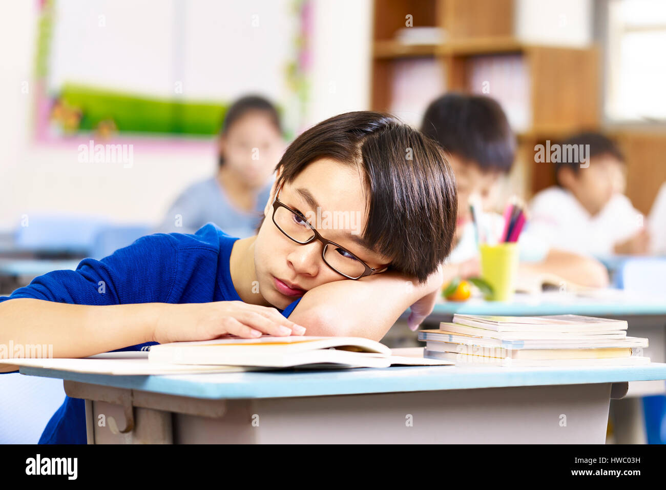 asiatische Grundschule junge seinen Kopf auf den Schreibtisch und denken ruht. Stockfoto