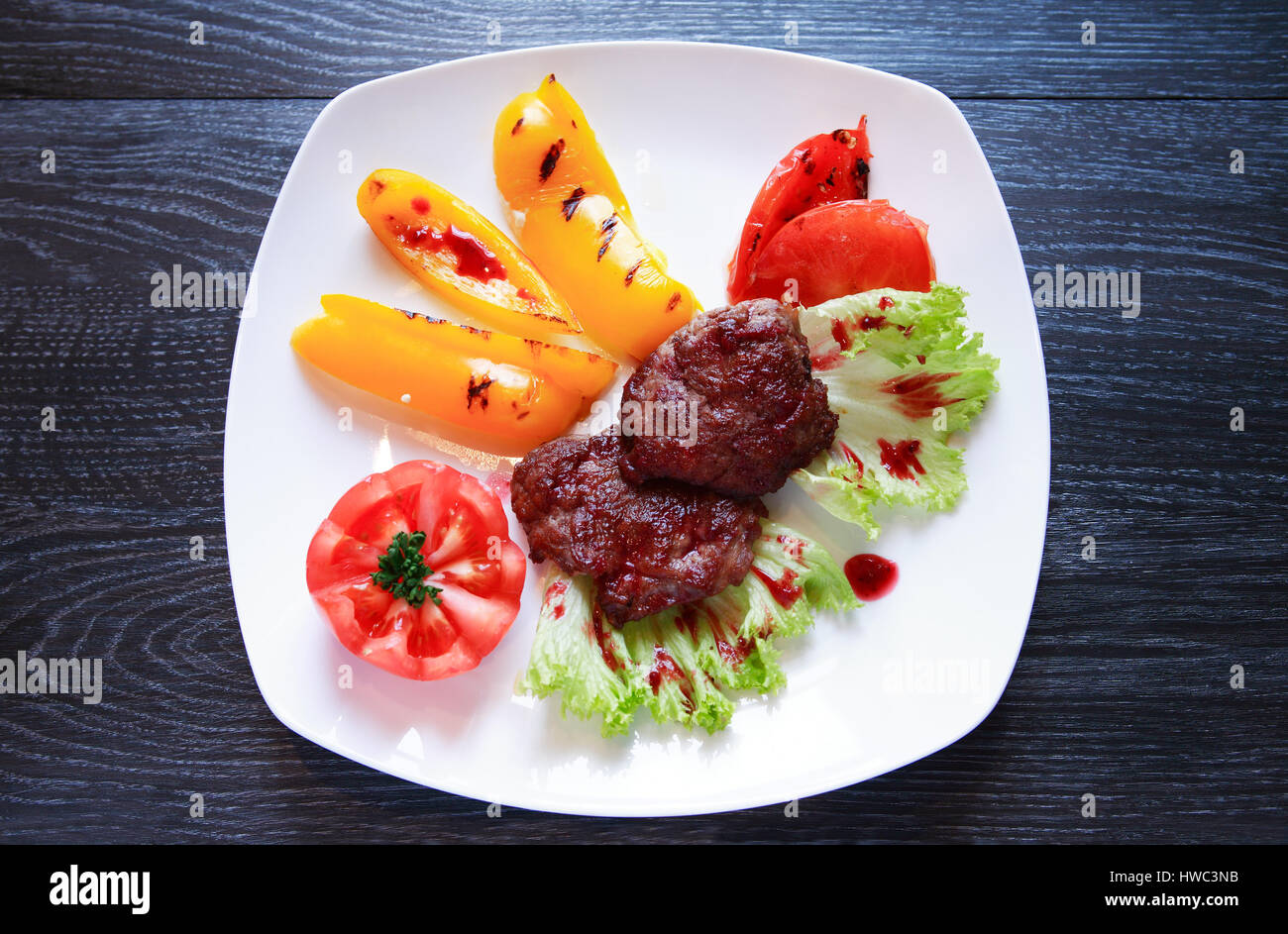 Teller mit gegrilltem Fleisch und Gemüse auf dunklen Holztisch Stockfoto