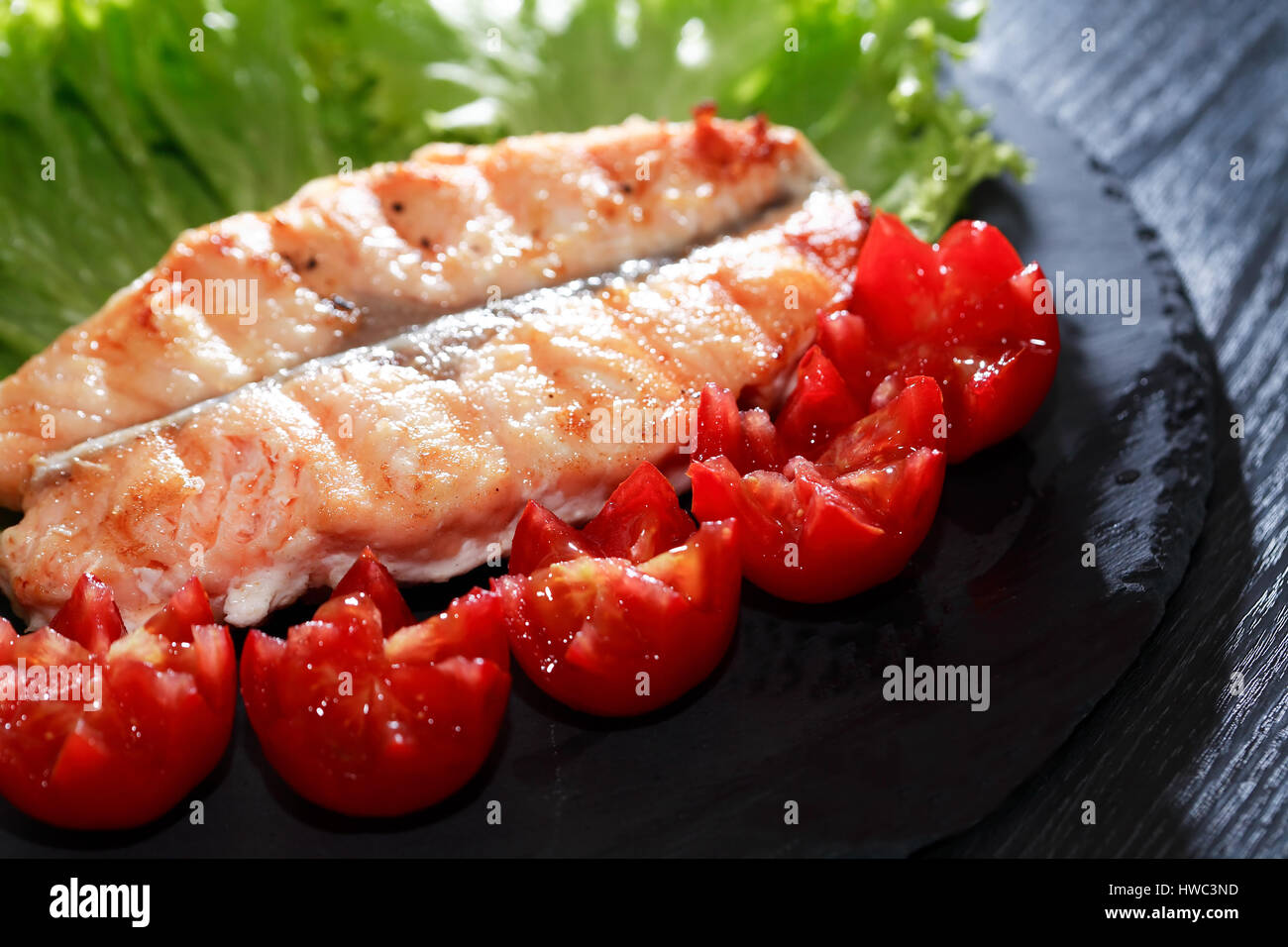 Teller mit gegrilltem Fisch und Gemüse auf dunklen Holztisch Stockfoto