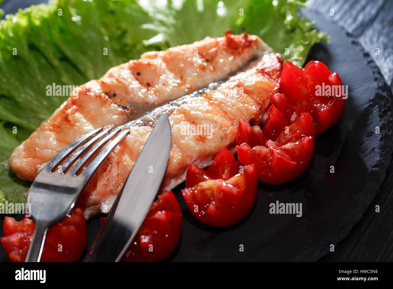 Teller mit gegrilltem Fisch und Gemüse auf dunklen Holztisch Stockfoto
