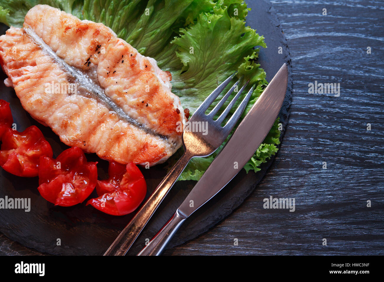 Teller mit gegrilltem Fisch und Gemüse auf dunklen Holztisch Stockfoto