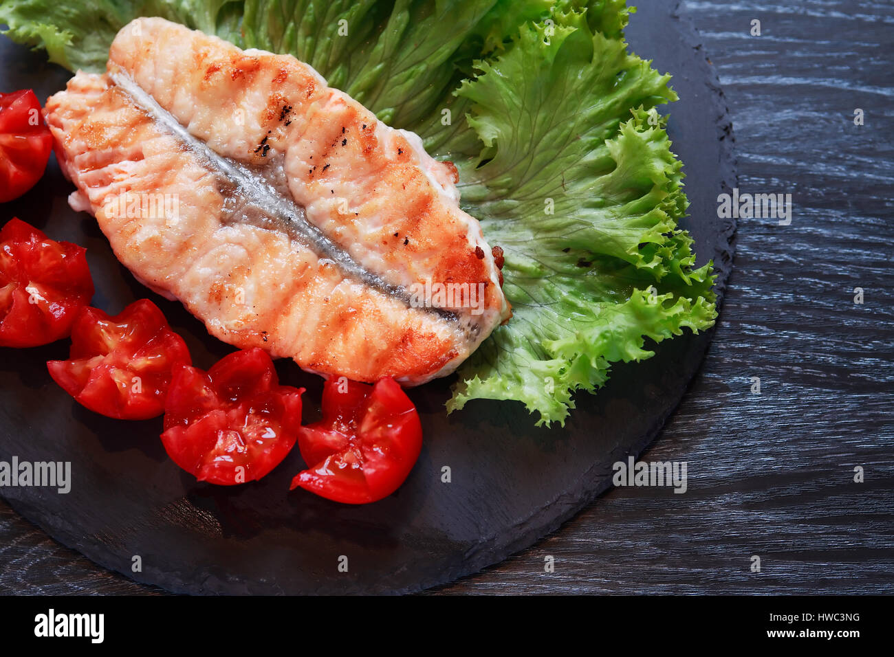 Teller mit gegrilltem Fisch und Gemüse auf dunklen Holztisch Stockfoto