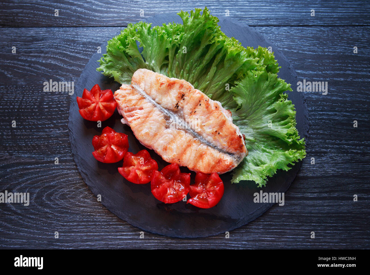 Teller mit gegrilltem Fisch und Gemüse auf dunklen Holztisch Stockfoto