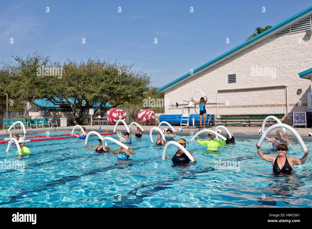 Gruppe von Frauen (verschiedenen Alters) Teilnahme an Wasser-Aerobic-Kurs, Ausbilder demonstriert, mit Styropor "Wasser Nudeln", Outdoor-beheizter Pool. Stockfoto