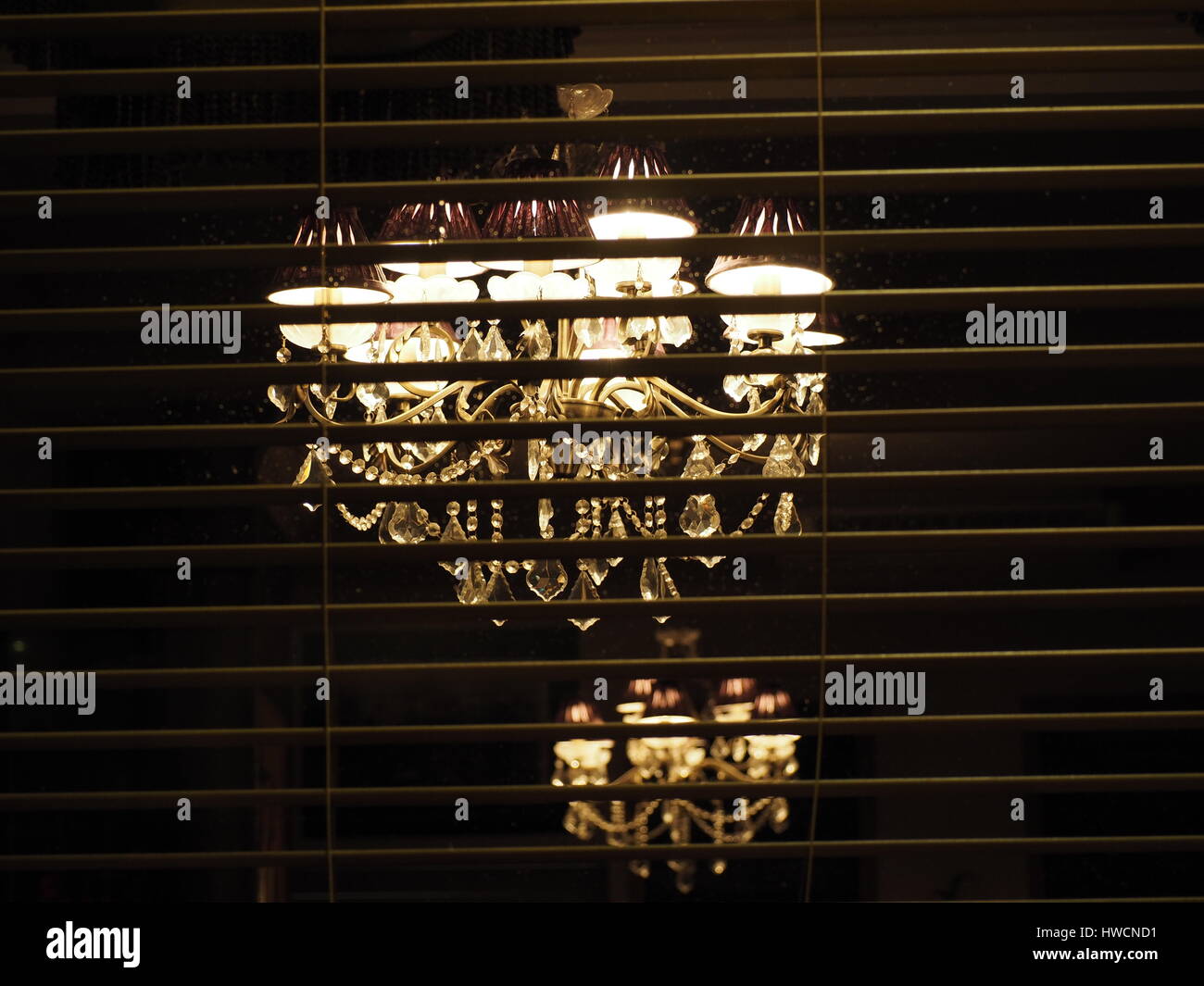 Zwei alte Kronleuchter aus Glas mit Kristall weißen Licht, eine scharf, einen weiteren streut darüber hinaus hinter modernen horizontalen Louvre blind beleuchtet Stockfoto