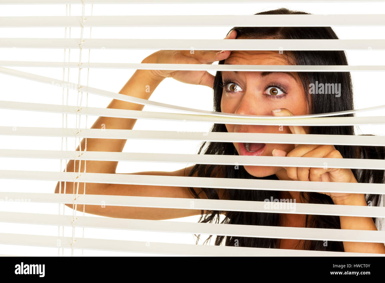 Eine junge Frau beobachtet etwas durch die Jalousie von ihrem Fenster, Eine Junge Frau Beobachtet Etwas Durch Die Jalousie Ihres Fensters Stockfoto