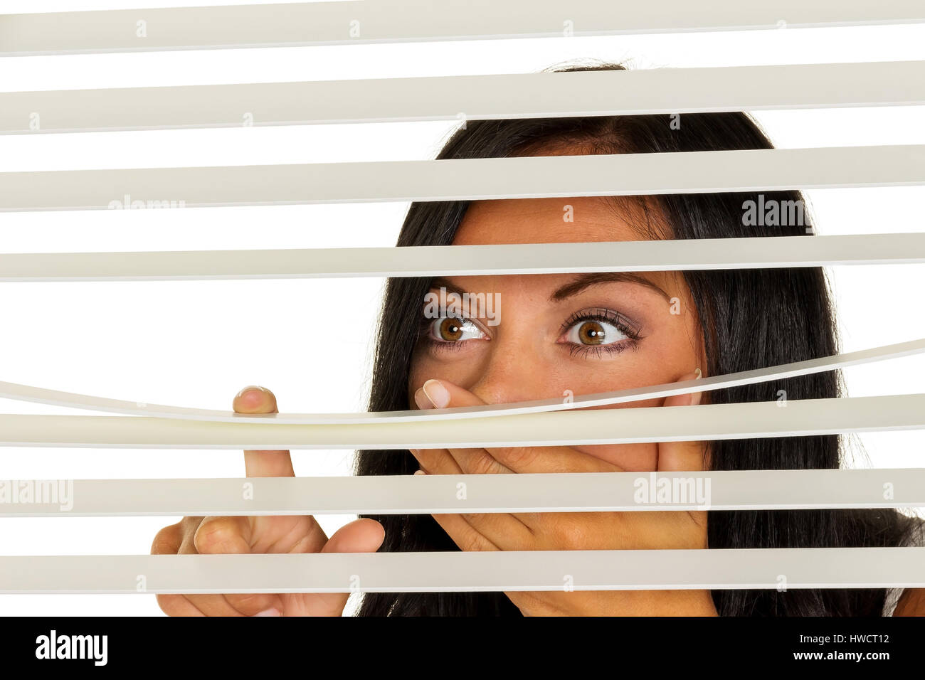 Eine junge Frau beobachtet etwas durch die Jalousie von ihrem Fenster, Eine Junge Frau Beobachtet Etwas Durch Die Jalousie Ihres Fensters Stockfoto