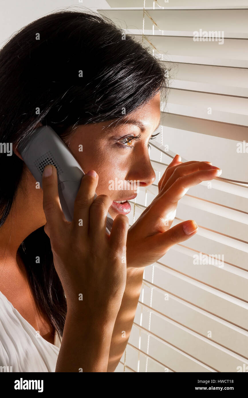 Eine junge Frau beobachtet etwas durch die Jalousie von ihrem Fenster, Eine Junge Frau Beobachtet Etwas Durch Die Jalousie Ihres Fensters Stockfoto