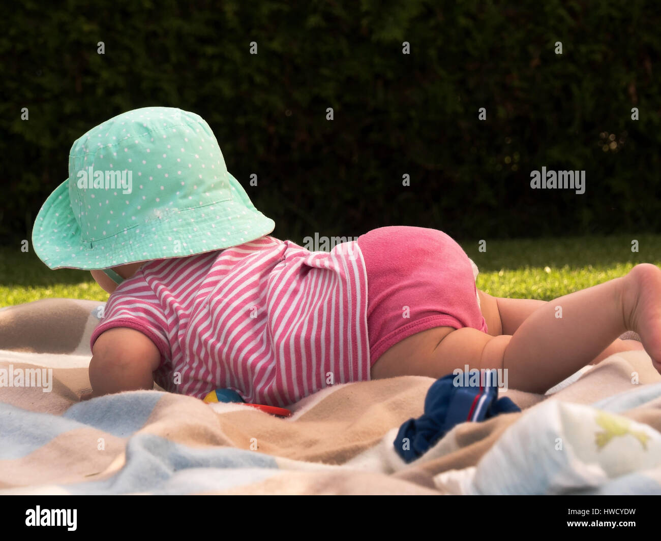 Ein Baby mit dem Bauch liegt und trägt einen Hut., Ein Baby Liegt am Bauch Und Hat Einen Hut Auf. Stockfoto