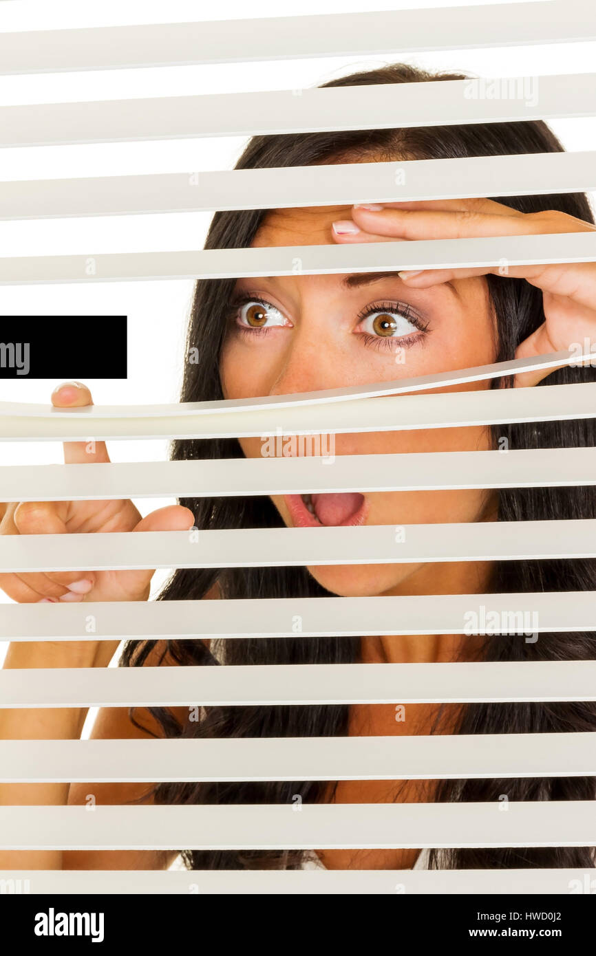 Eine junge Frau beobachtet etwas durch die Jalousie von ihrem Fenster, Eine Junge Frau Beobachtet Etwas Durch Die Jalousie Ihres Fensters Stockfoto