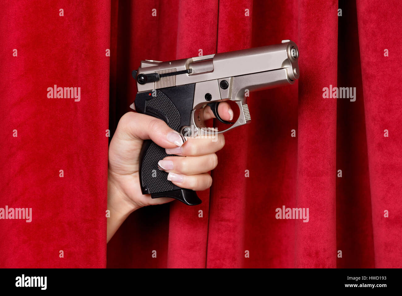 Ein Revolver ist ein Frauen Handarbeit von einem roten Vorhang, Eine Revolver Wird von Einer Frauenhand Durch Einen Roten Vorhang Geschoben geschoben. Stockfoto