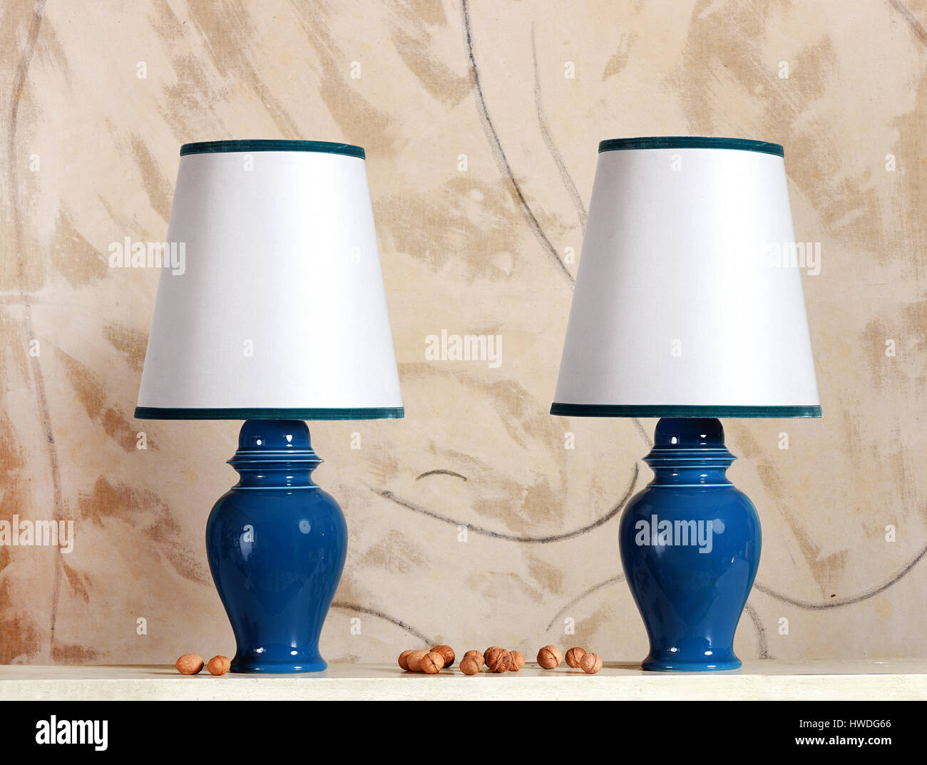 Paar blaue Keramik elektrische Lampen mit weißen Schattierungen getrimmt in einem passenden Blau steht auf einem Tisch mit ganzen frischen Walnüssen Stockfoto