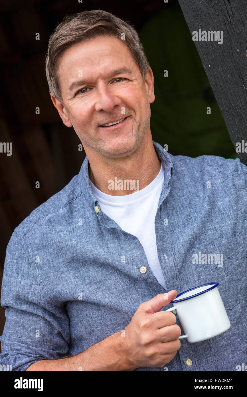 Porträt gedreht von einem attraktiven, erfolgreichen und glücklichen Mann mittleren Alters männlichen trägt ein blaues Hemd trinken Tee oder Kaffee aus einer Blechtasse Stockfoto