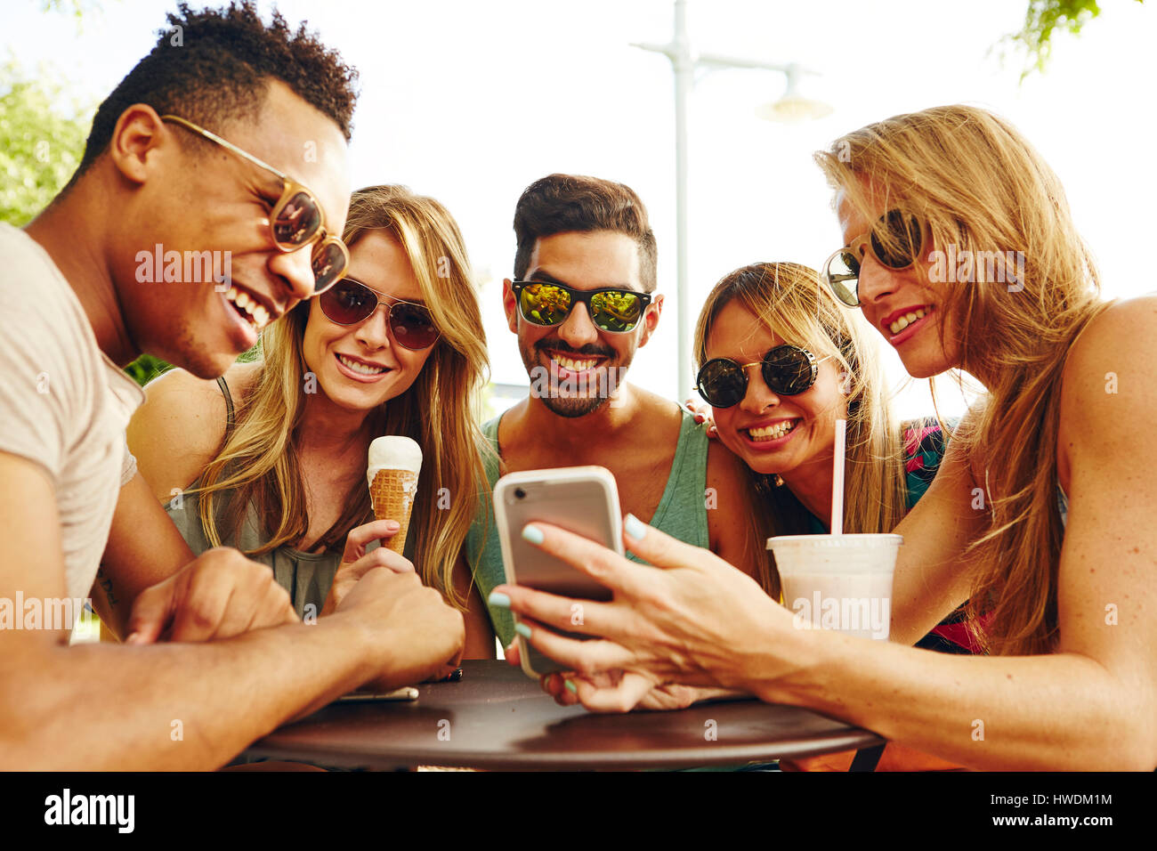 Fünf Erwachsene Freunde betrachten Smartphone am Park Tisch Stockfoto