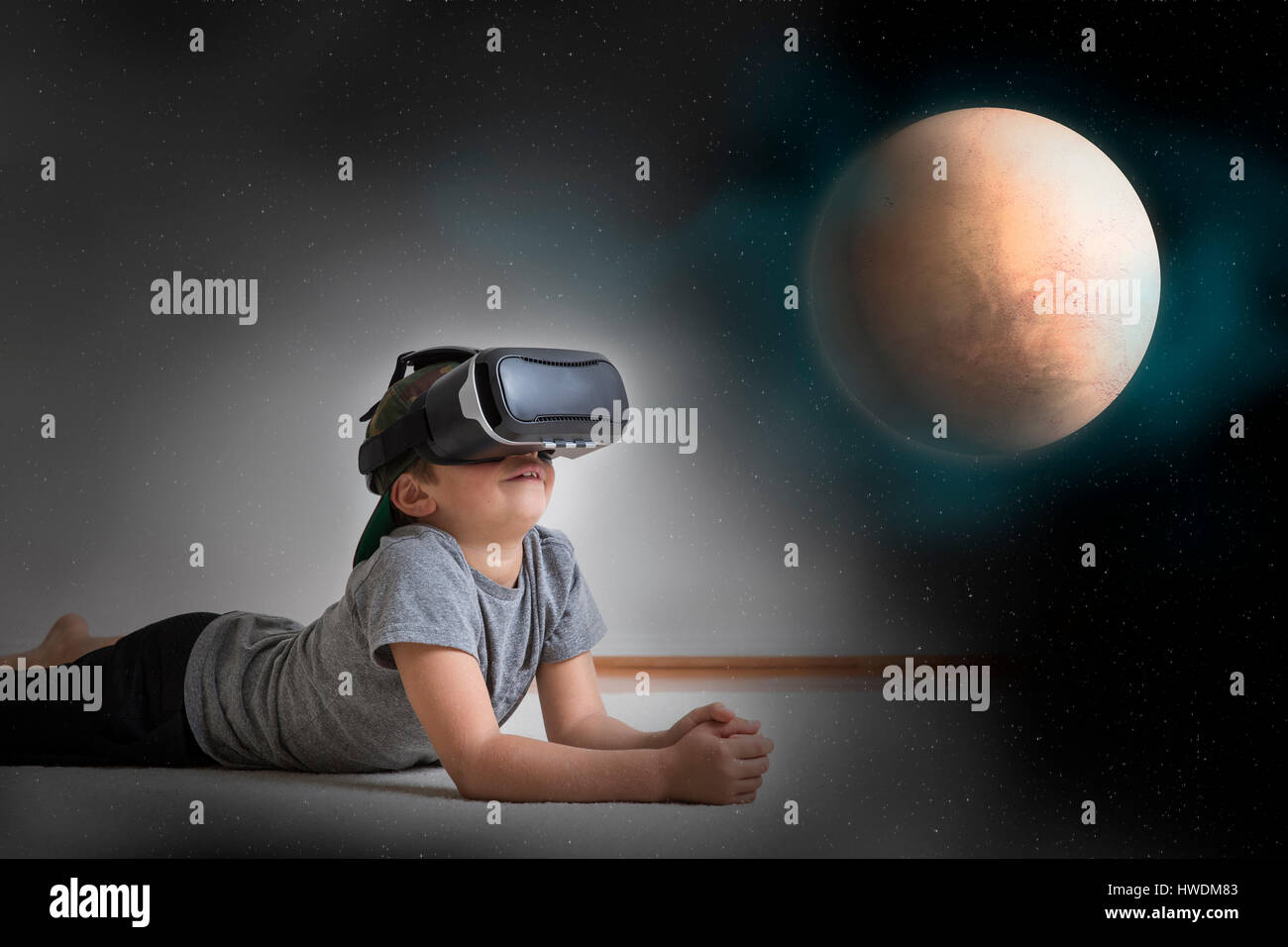 Kleiner Junge am Boden liegend, virtual-Reality-Kopfhörer tragen, mit Blick auf Planeten, digital composite Stockfoto