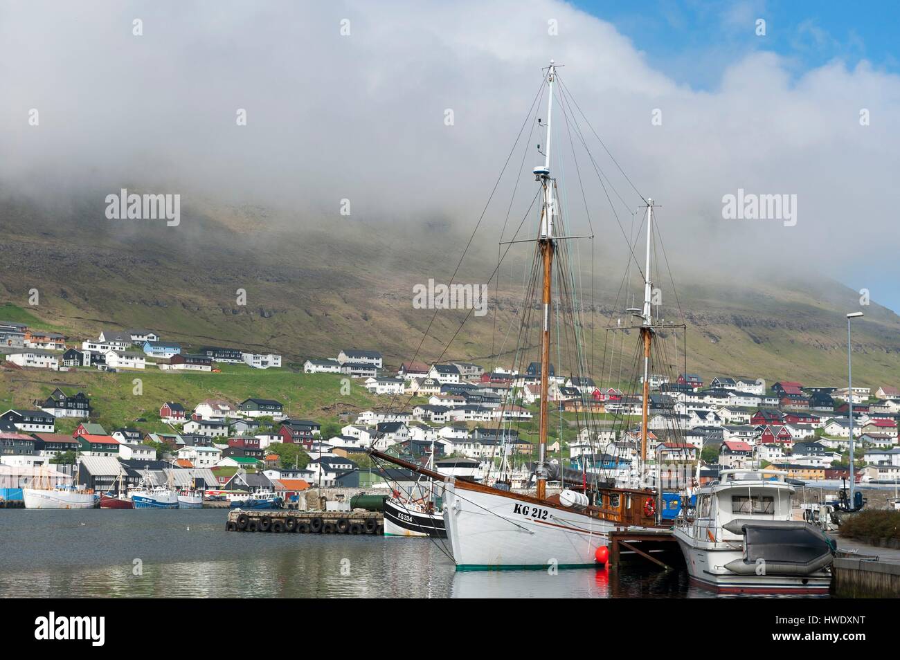 Dänemark, Färöer Inseln, Insel Bordoy, Klaksvik, Schoner aus Holz in den Hafen, Stadt und Berge, Wolken im Hintergrund Stockfoto
