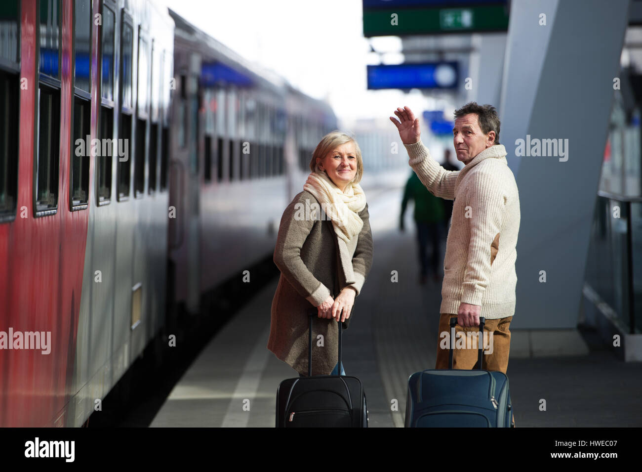 Älteres Paar auf Zug station ziehen Trolley Gepäck winken. Stockfoto