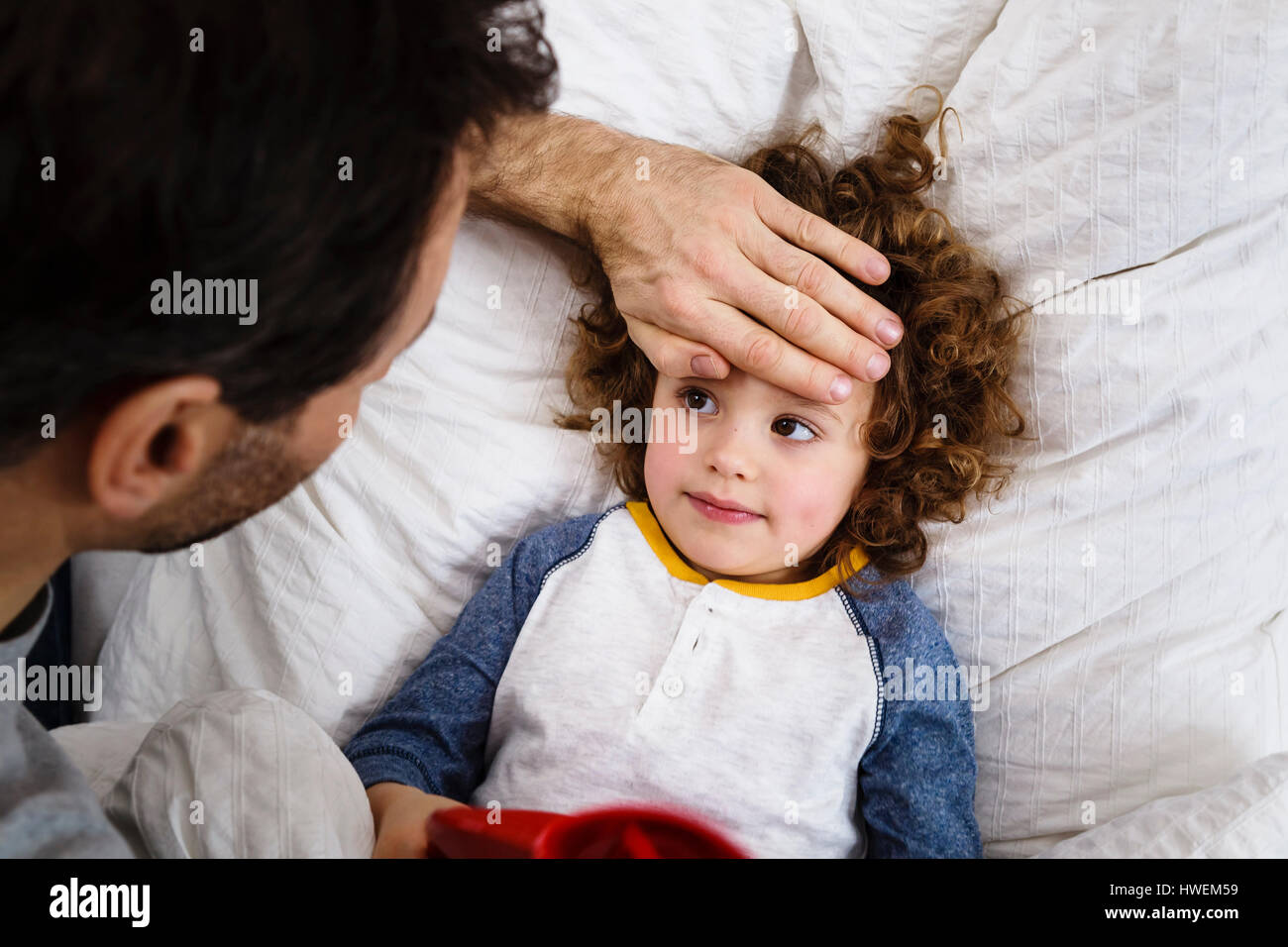 Draufsicht der Mädchen im Bett mit Vaters Hand auf Stirn Stockfoto